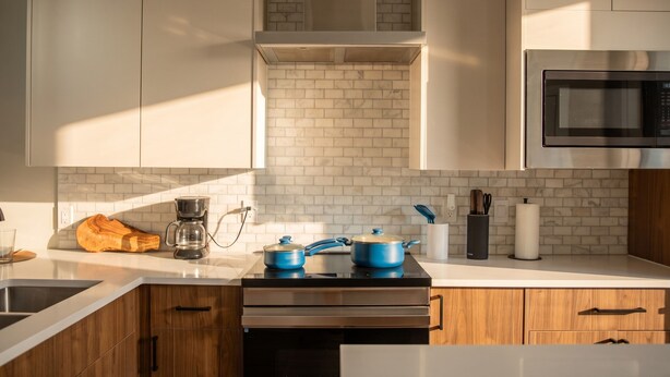 Une cuisine moderne avec des meubles blancs, un plan de travail noir, une machine à café, une casserole bleue et un four à micro-ondes.