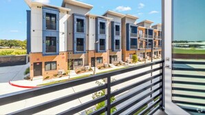 Un immeuble résidentiel moderne à plusieurs étages, doté de balcons, avec un ciel dégagé et une pelouse bien entretenue.