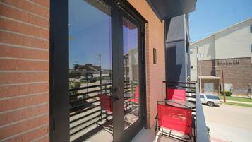 Un balcon avec une porte vitrée, des chaises rouges et une vue sur un parking et des immeubles.