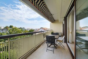 Ein Balkon mit Tisch und Stühlen, Blick auf die Stadtlandschaft und ein gestreifter Jalousie.