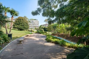 A paved pathway in a landscaped area with benches, surrounded by greenery and a multi-story building in the background. - Apartment '3 Pièces Cannes' with Shared Terrace, Wi-Fi and Air Conditioning (Cannes)