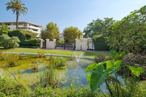 A serene garden with a pond, lush greenery, and a building in the background. - Apartment '3 Pièces Cannes' with Shared Terrace, Wi-Fi and Air Conditioning (Cannes)