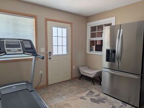 Una cocina compacta con refrigerador, caminadora y ventana con persianas.