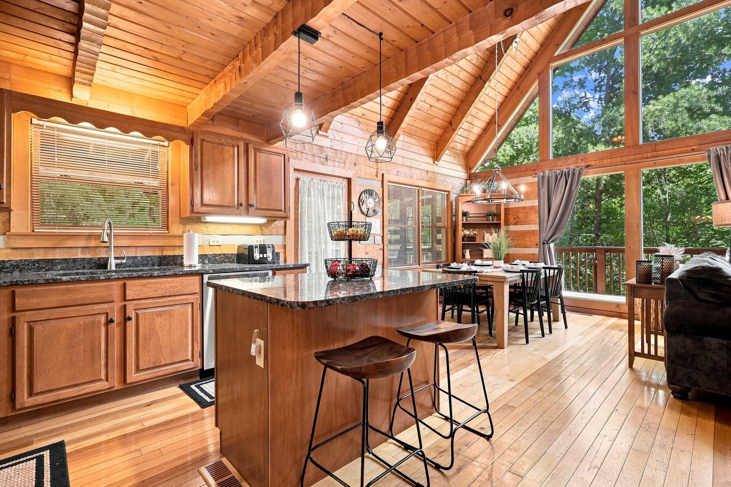 A spacious kitchen with wooden cabinets, a central island with bar stools, and large windows offering a view of the outdoors.