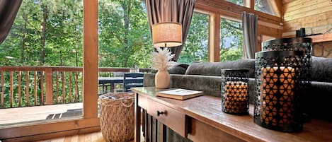 A cozy cabin interior with a wooden deck, a sofa, a table with a lamp, and decorative items.