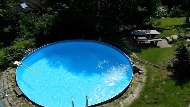 A circular swimming pool with a clear blue surface, surrounded by a stone pathway and greenery. - Apartment 'Fewo Ruthe' (Wehr)
