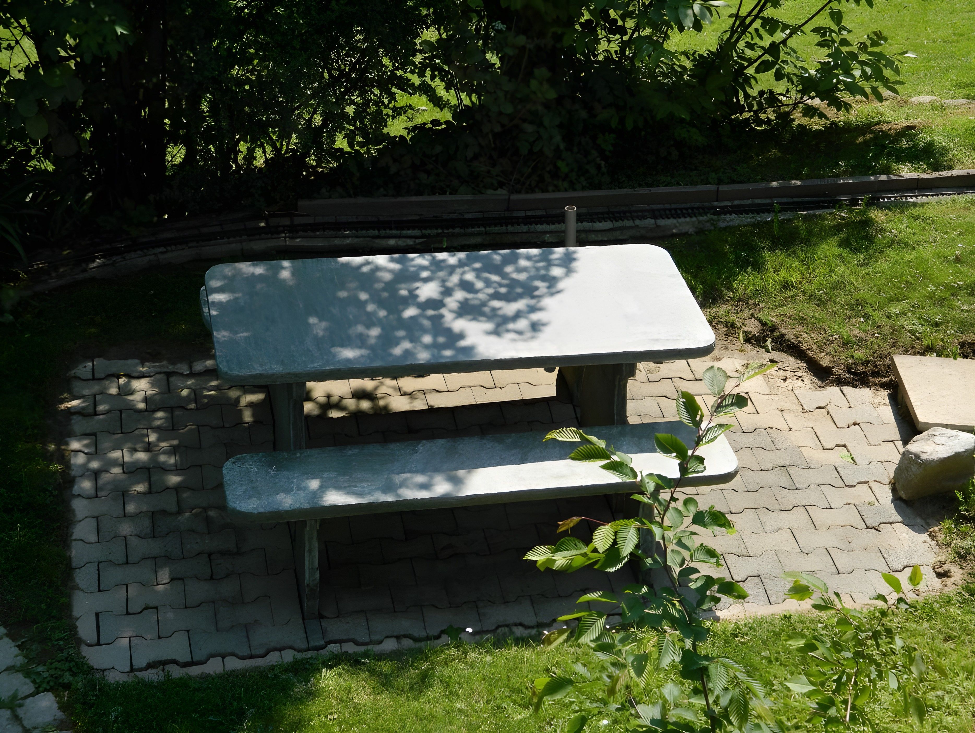A picnic table with a bench, surrounded by a brick pathway and greenery.