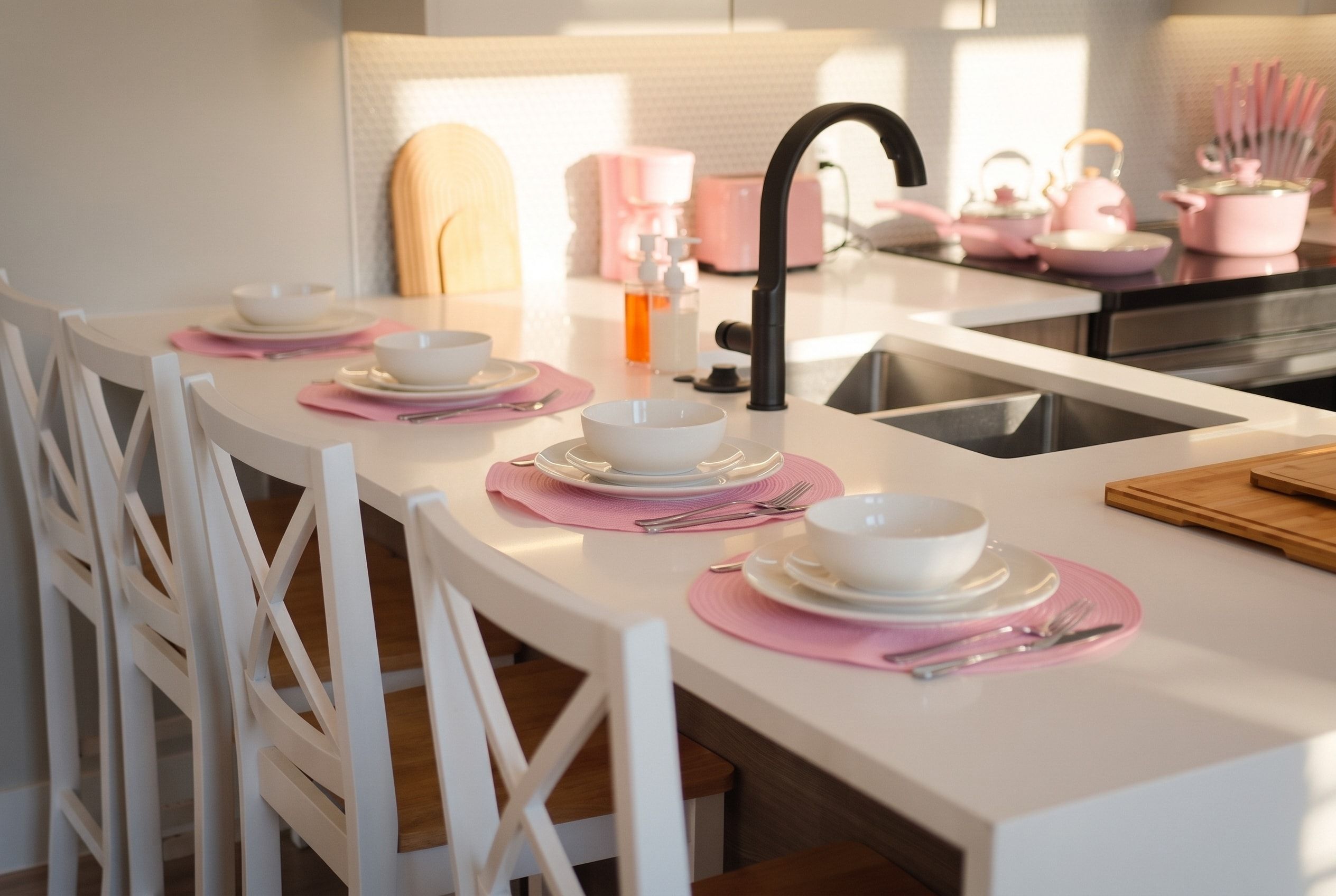 Une cuisine moderne avec des meubles blancs, un îlot central agrémenté de sets de table roses et un robinet noir.