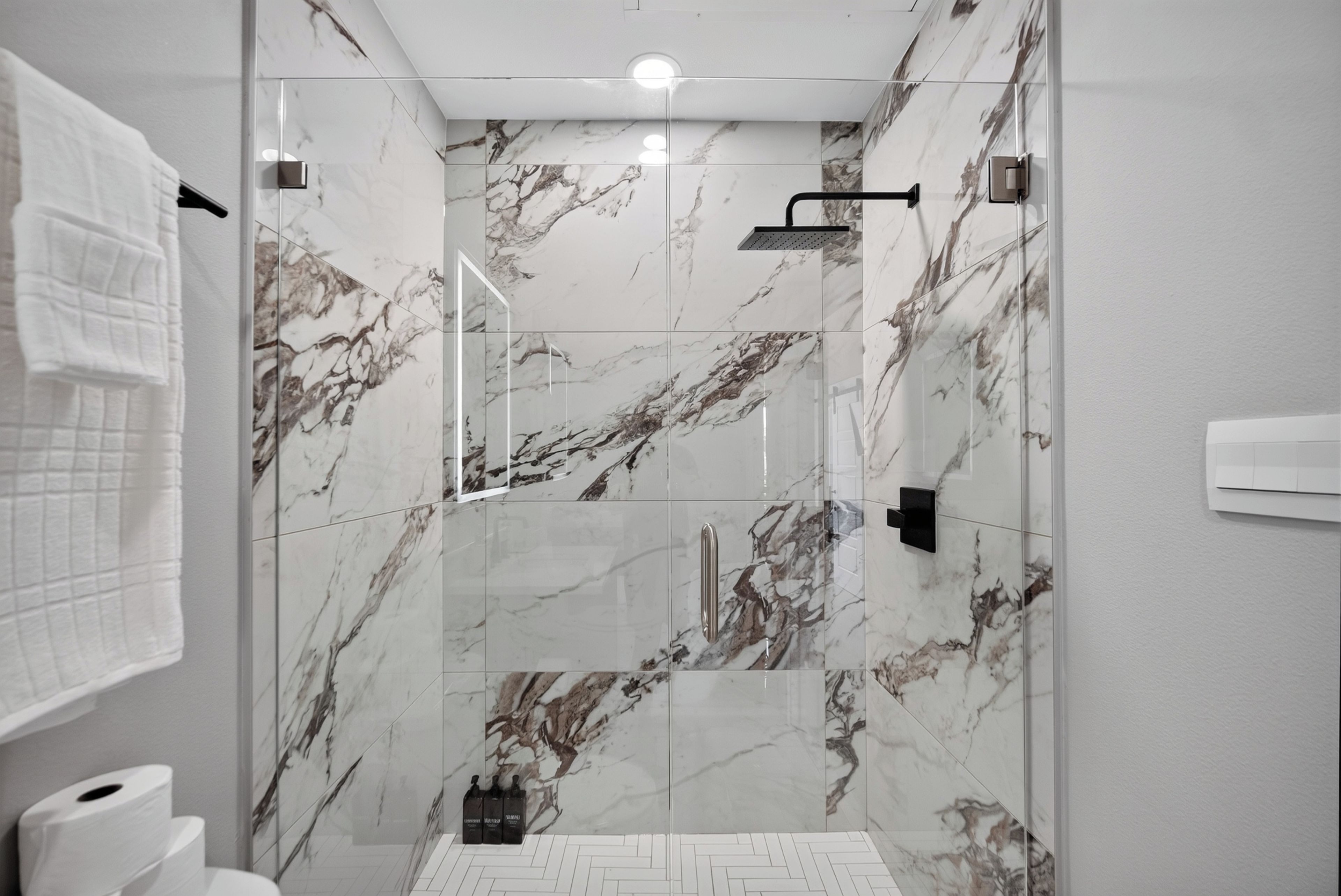 A modern bathroom with marble walls, a shower, and a toilet.