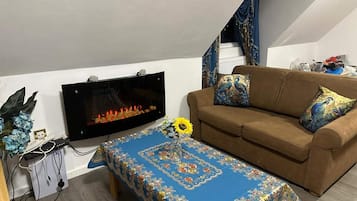 Uma sala de estar com sofá, mesa de centro, televisão de tela plana e lareira.