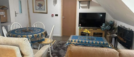 A cozy living room with a dining area, a flat-screen TV, and a door leading to another room.