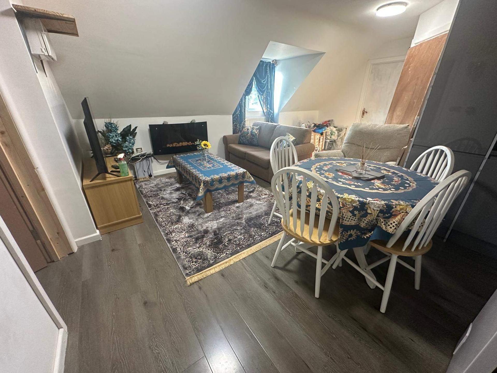 A compact living space with a dining table, two chairs, a sofa, and a TV mounted on the wall.