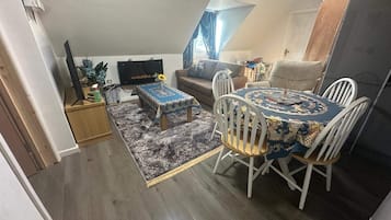 Espaço compacto com mesa de jantar, duas cadeiras, sofá e televisão fixada na parede.