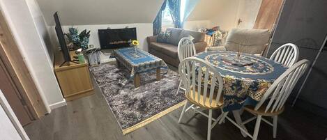 Un espacio habitable funcional con una mesa de comedor, dos sillas, un sofá y un televisor montado en la pared.