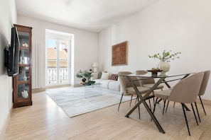 A modern living room with a glass coffee table, beige chairs, a white sofa, and a TV mounted on the wall. - Charming 2-bedroom apartment in La Latina (Madrid)