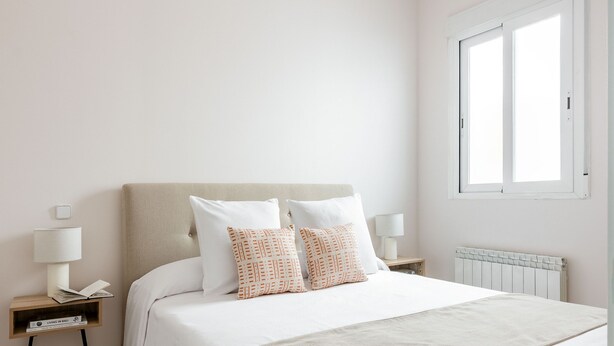 Une chambre à coucher avec un lit, des tables de chevet, une lampe, un radiateur et une fenêtre.