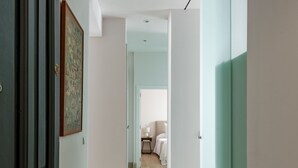 Un couloir avec un plancher en bois, une porte sombre et un mur de couleur claire orné d’un tableau encadré.
