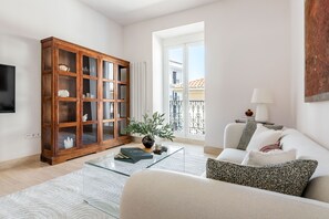 Ein modernes Wohnzimmer mit einem Holzkabinett, einem Glastisch, einem weißen Sofa und Blick auf einen Balkon.