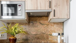 Une cuisine avec des meubles en bois, un four à micro-ondes, un dosseret en granit, une plante et des récipients à sel.