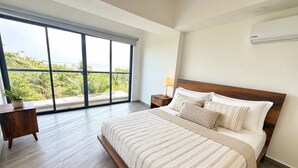 A bedroom with a large window, a bed with striped bedding, a nightstand, and an air conditioning unit. - Luxurious 2BR Ocean View Condo Rooftop Pool and Jacuzzi (Cartagena de Indias)