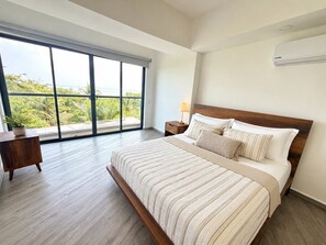 Une chambre avec une grande fenêtre, un lit avec une literie à rayures, une table de chevet et un appareil de climatisation.