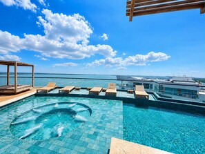 Ein Pool mit Endlos-Effekt auf dem Dach, mit Holzliegen und einem Whirlpool, mit Blick auf ein Gewässer.