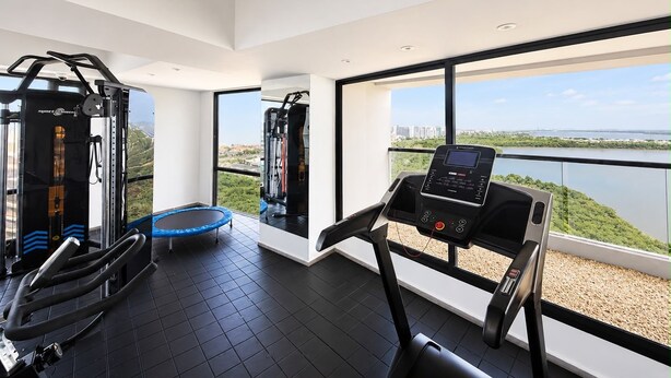 A gym with exercise equipment, a trampoline, and a treadmill with a view of a lake and buildings. - Luxurious 2BR Ocean View Condo Rooftop Pool and Jacuzzi (Cartagena de Indias)