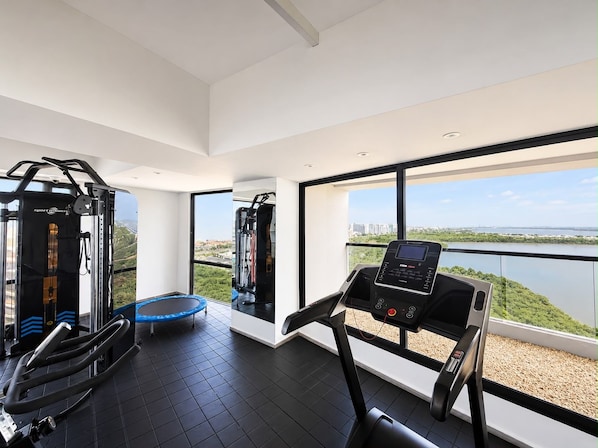Ein Fitnessraum mit Trainingsgeräten, einer Hüpfburg und einem Laufband mit Blick auf einen See und Gebäude.