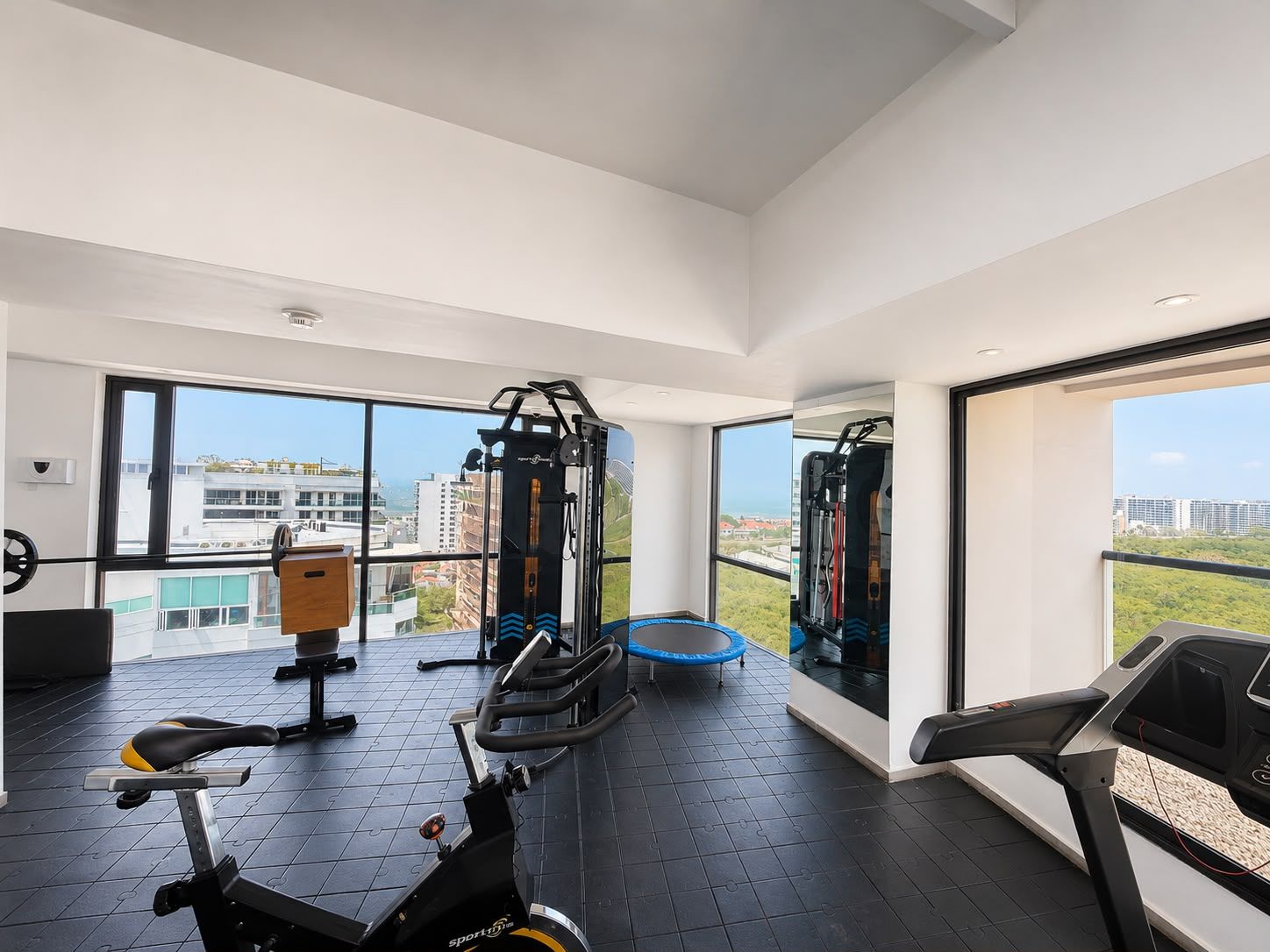 A modern gym with exercise equipment, large windows, and a view of the city.