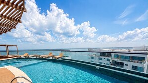 A rooftop infinity pool with wooden deck and lounge chairs, overlooking a cityscape. - Luxurious 2BR Ocean View Condo Rooftop Pool and Jacuzzi (Cartagena de Indias)