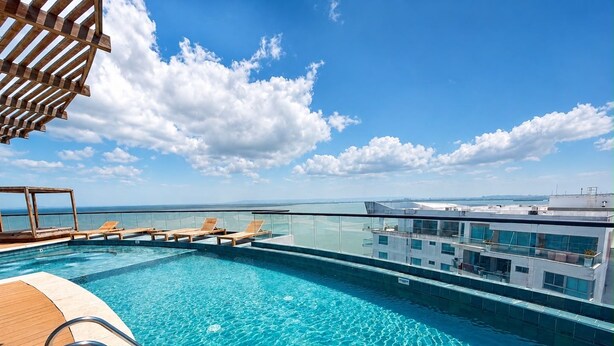 A rooftop infinity pool with clear blue water, wooden deck, and lounge chairs. - Luxurious 2BR Ocean View Condo Rooftop Pool and Jacuzzi (Cartagena de Indias)