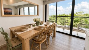 A dining area with a wooden table, chairs, and a large window with a view of greenery. - Luxurious 2BR Ocean View Condo Rooftop Pool and Jacuzzi (Cartagena de Indias)