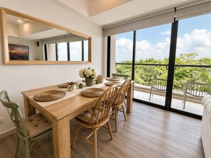 Un espace repas comprenant une table en bois, des chaises et une grande fenêtre donnant sur un paysage verdoyant.
