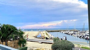 Uma marina com barcos, uma praia de areia e céu claro.