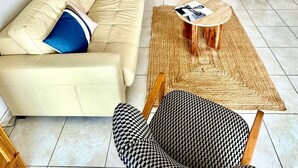 Sala de estar com sofá, poltrona estampada, mesa de centro e estante com objetos decorativos.
