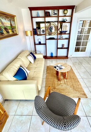 Un salon comprenant un canapé, un fauteuil à motifs, une table basse et une bibliothèque agrémentée d’objets décoratifs.
