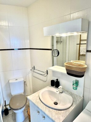 Casa de banho com sanita, lavatório, espelho e porta-toalhas.