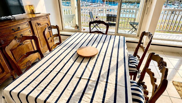 Uma sala de jantar com uma mesa coberta por toalha listrada, cadeiras de madeira, um armário de madeira e uma televisão em cima.