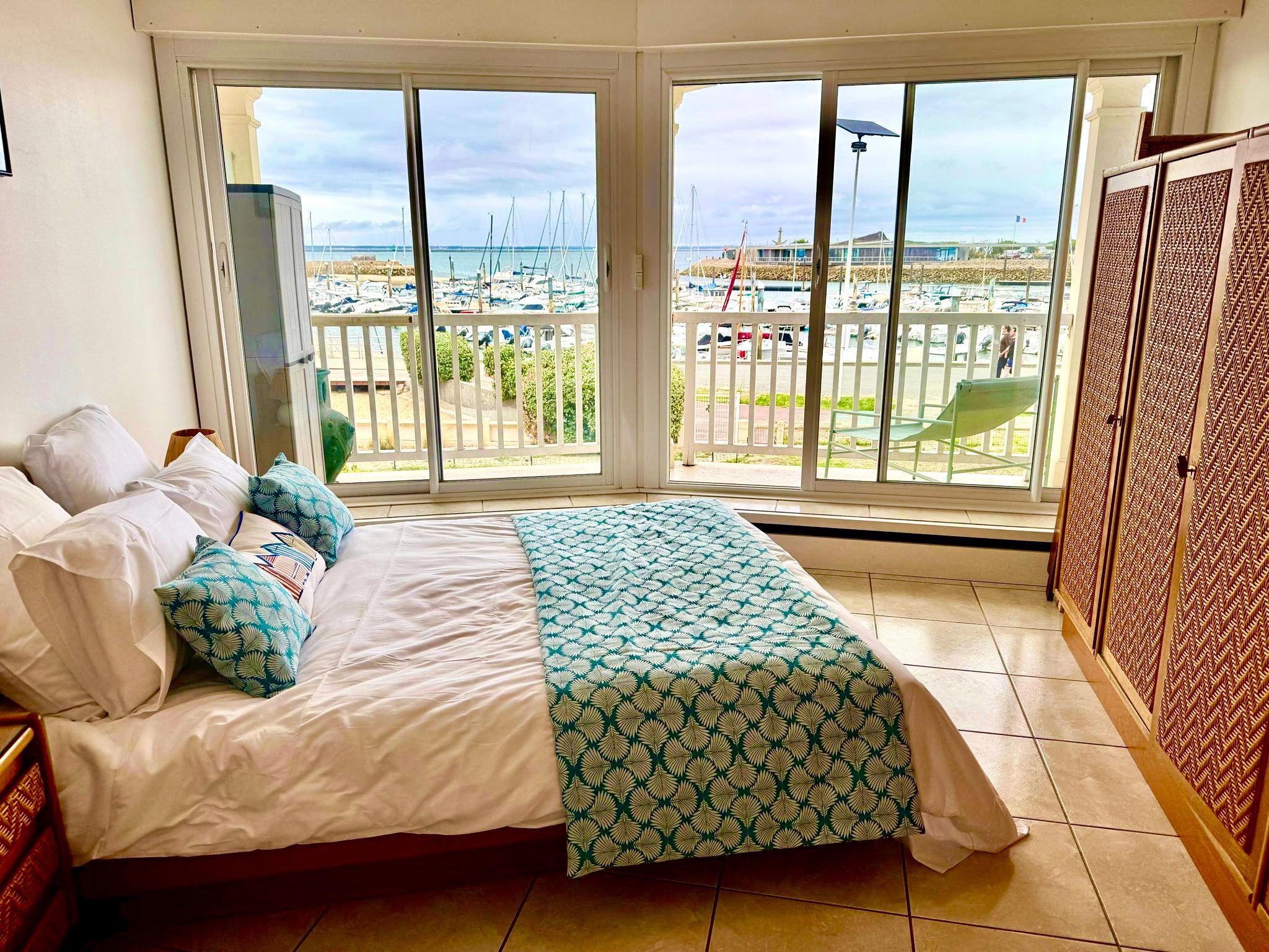 A bedroom with a bed, a view of a marina, and a balcony with a view of the marina.