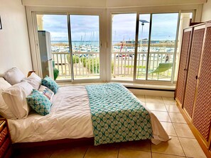 Quarto com cama, vista para um porto de iates e varanda com vista para o porto.