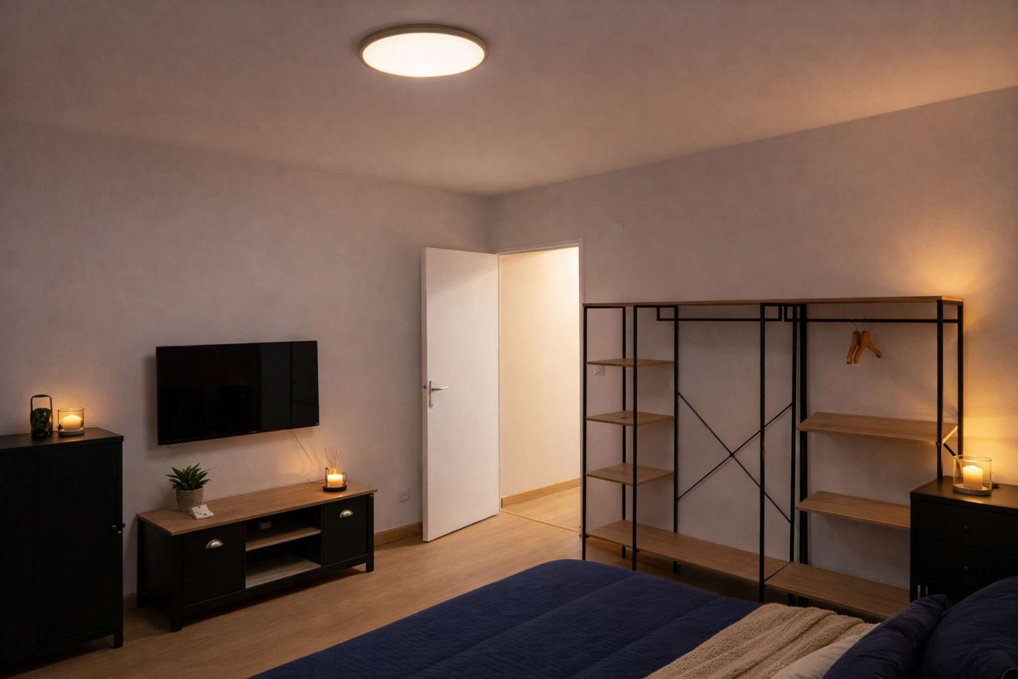 Een slaapkamer met een bed, een televisie, een kledingkast en een nachtkastje met een kaars.