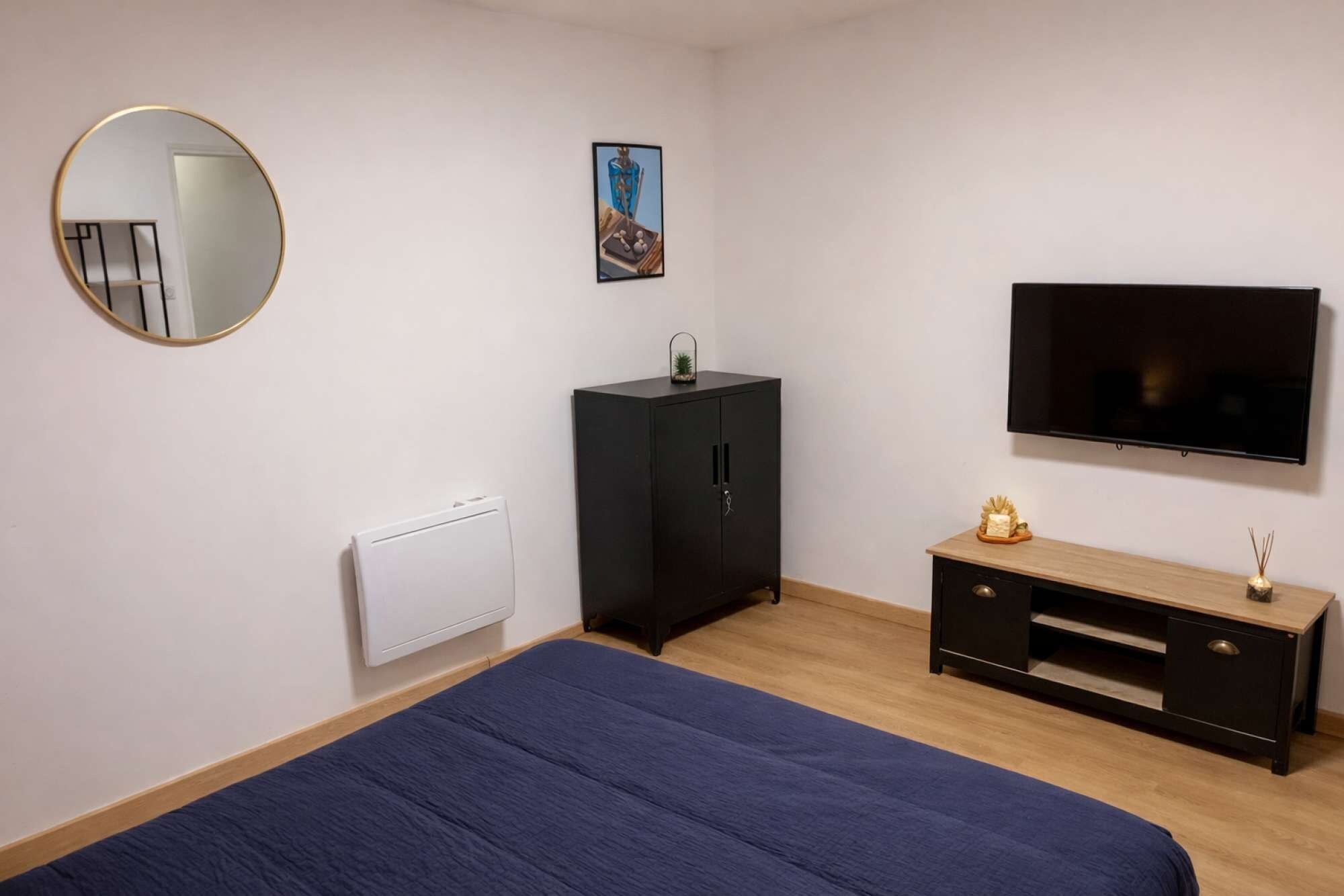 Een slaapkamer met een bed, een kledingkast, een radiator, een televisie en een klein plankje met decoratieve spullen.