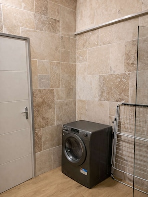 Une petite buanderie équipée d’un lave-linge, d’un étendoir métallique et d’une porte.