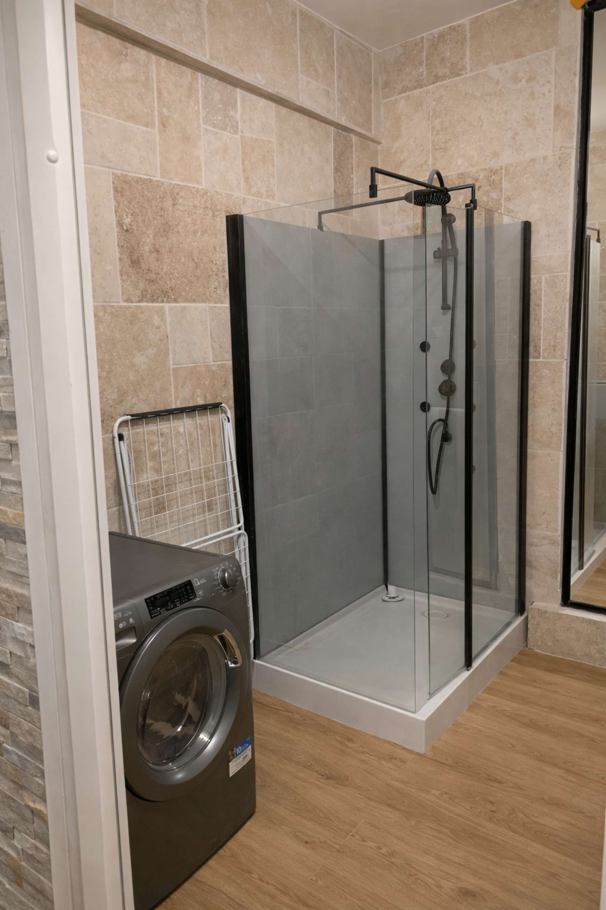 Une salle de bain moderne dotée d’une douche à parois de verre, d’un lave-linge encastré et d’un sol carrelé.