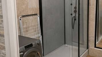 Une salle de bain moderne dotée d’une douche à parois de verre, d’un lave-linge encastré et d’un sol carrelé.