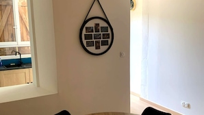 A round wooden table with a yellow object in the center, surrounded by black chairs, in a room with a wall-mounted picture frame. - Le Cocon de Sohën – A Cozy and Comfortable Two-Bedroom Apartment in Montréjeau (MONTREJEAU)
