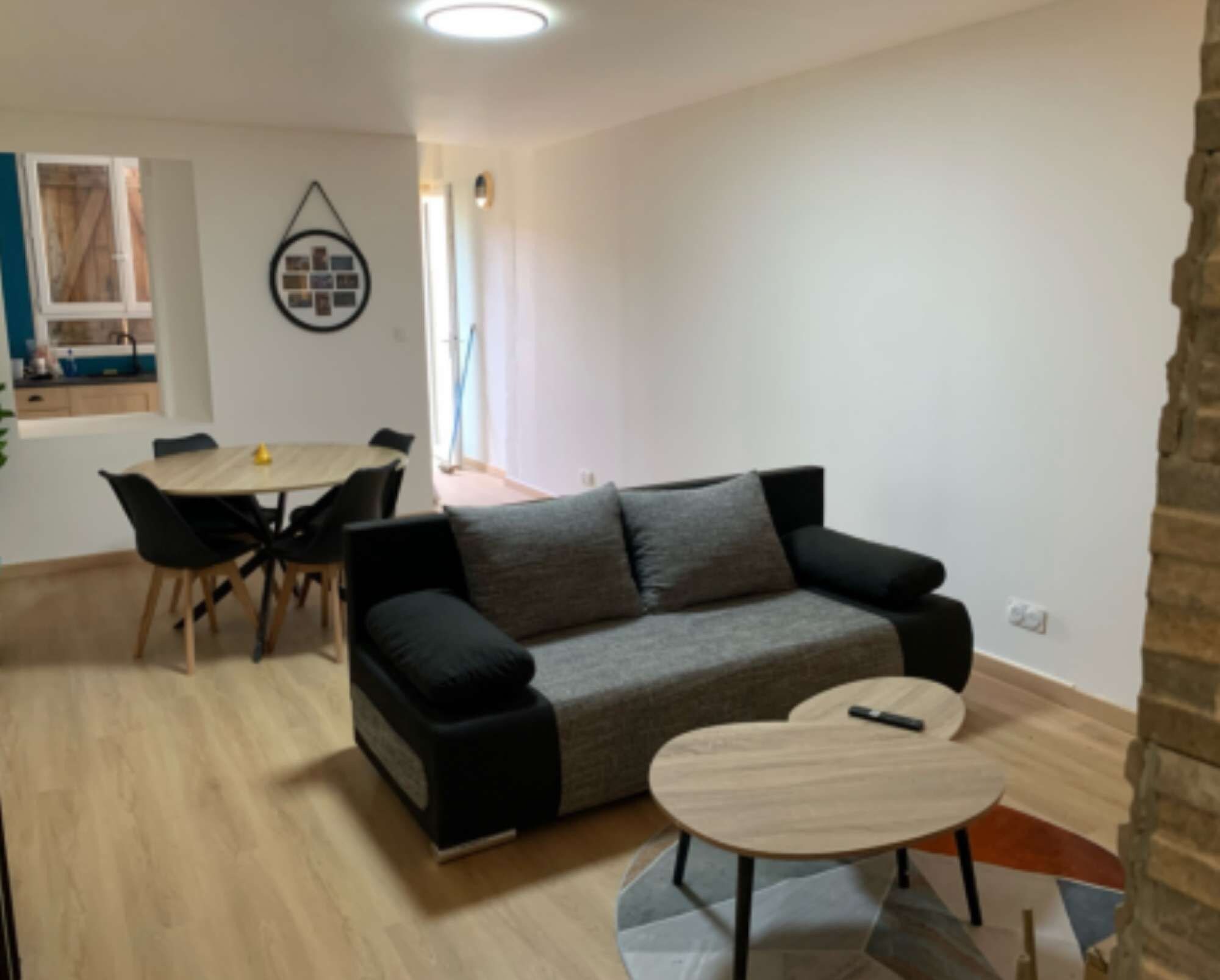 Een moderne woonkamer met een grijze bank, een ronde salontafel en een eethoek met een tafel en stoelen.