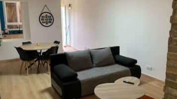 Een moderne woonkamer met een grijze bank, een ronde salontafel en een eethoek met een tafel en stoelen.