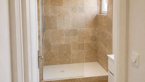Un baño con ducha, paredes de azulejos, suelo de madera y ventana.