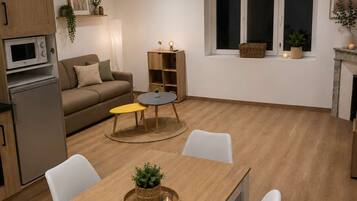 Une cuisine moderne dotée d’appareils électroménagers intégrés, un coin repas avec une table et des chaises en bois, un canapé et une petite table d’appoint.